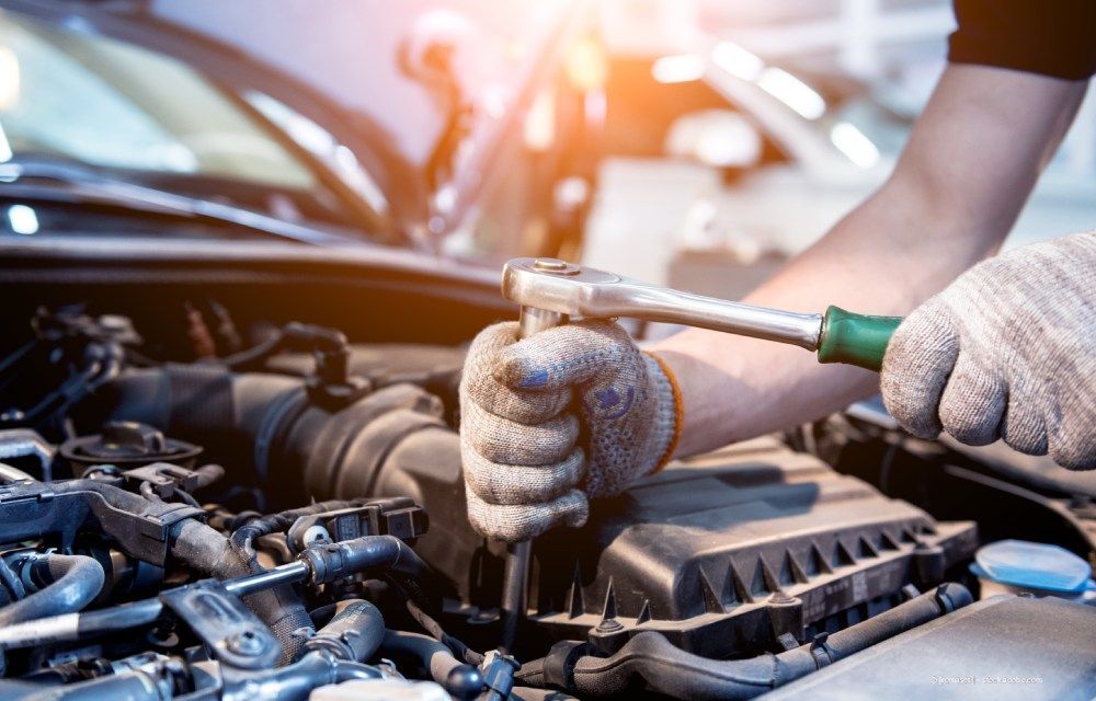 Die behandschuhten Hände eines Mechanikers benutzen in einer Garage einen Ratschenschlüssel an einem Automotor.