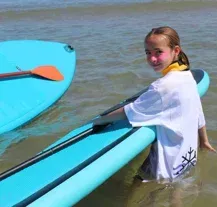 Una niña sostiene una tabla de surf en el agua.