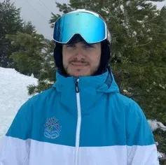 Un hombre que lleva una chaqueta azul y blanca y gafas protectoras está de pie en la nieve.