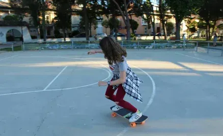 Una niña está montando una patineta en una cancha de baloncesto.
