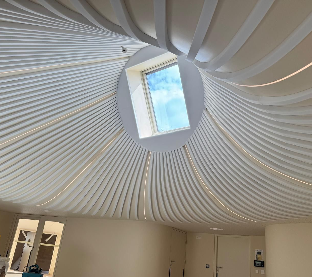 Grille de plafond blanche avec supports métalliques apparents, partiellement recouverte de panneaux beiges.