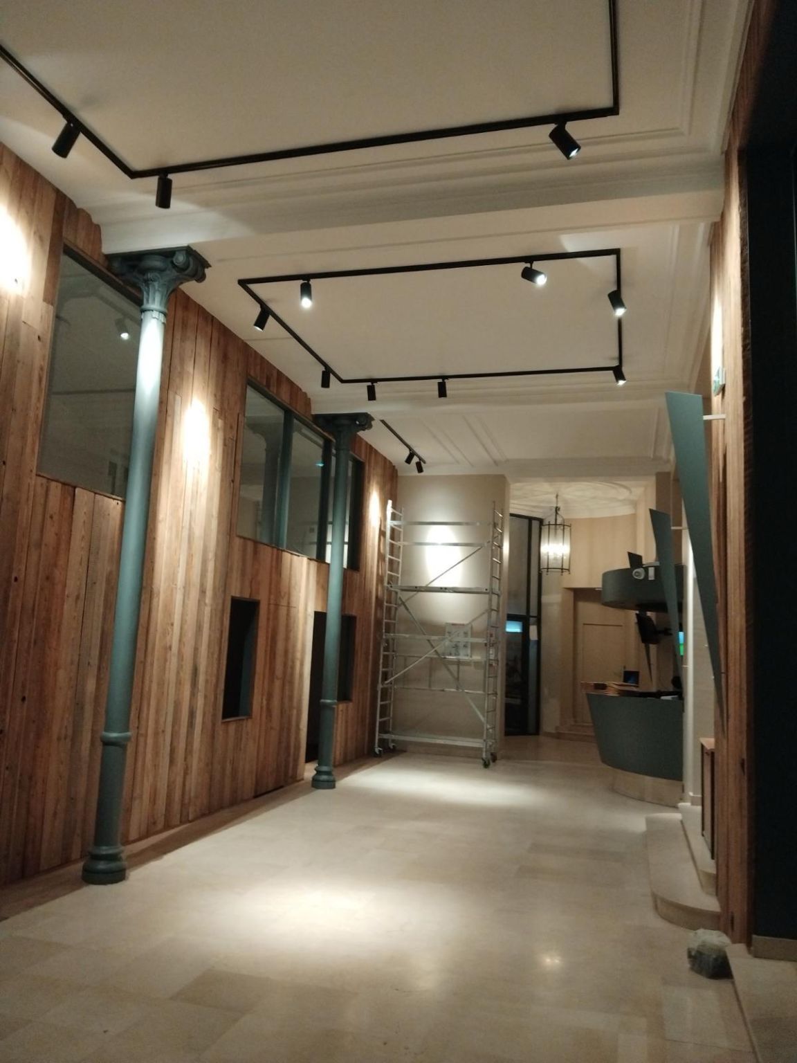 Long couloir avec boiseries, colonnes, éclairage sur rail et échafaudage roulant.