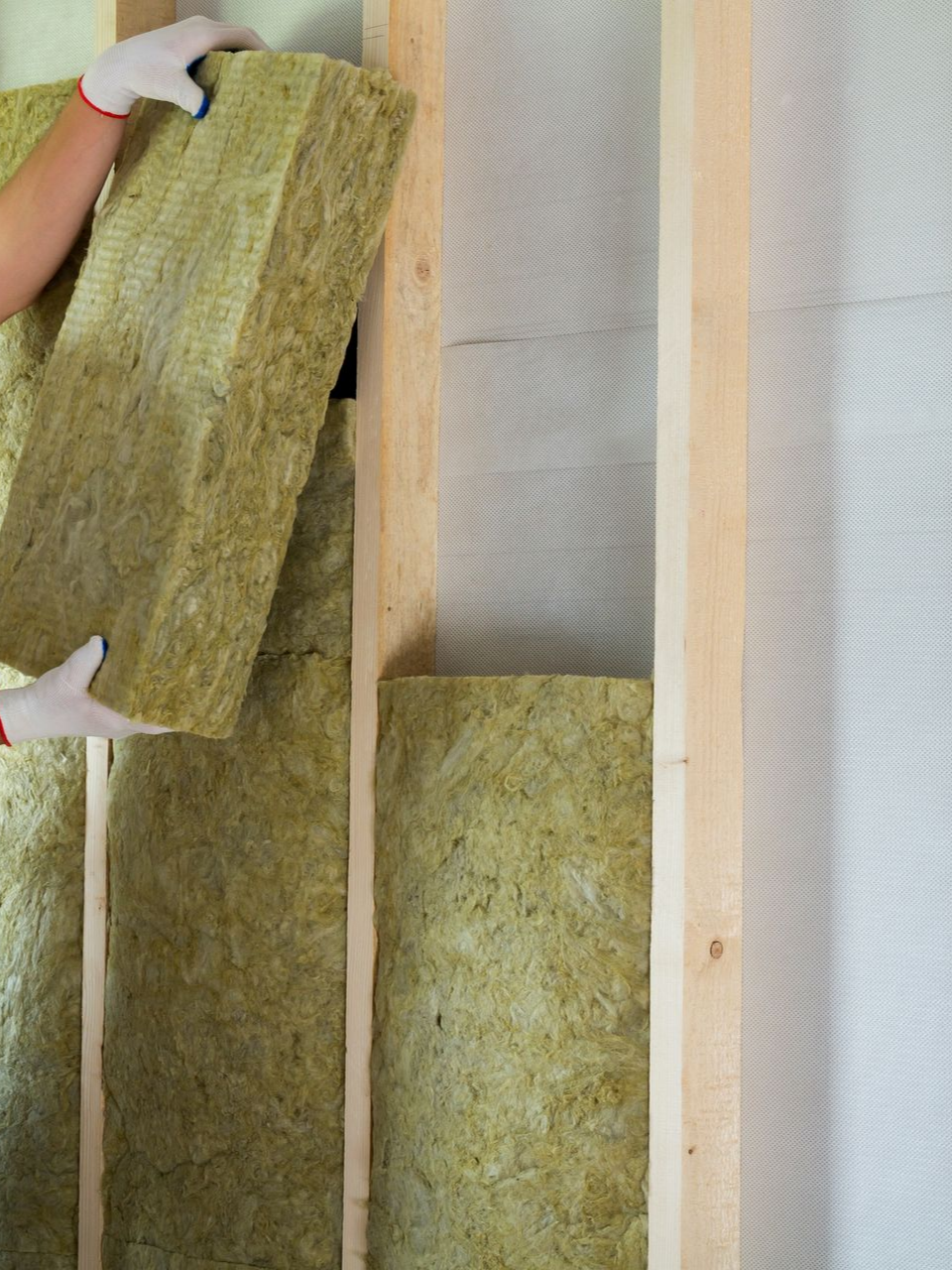 Personne installant de l'isolant entre des montants muraux en bois.