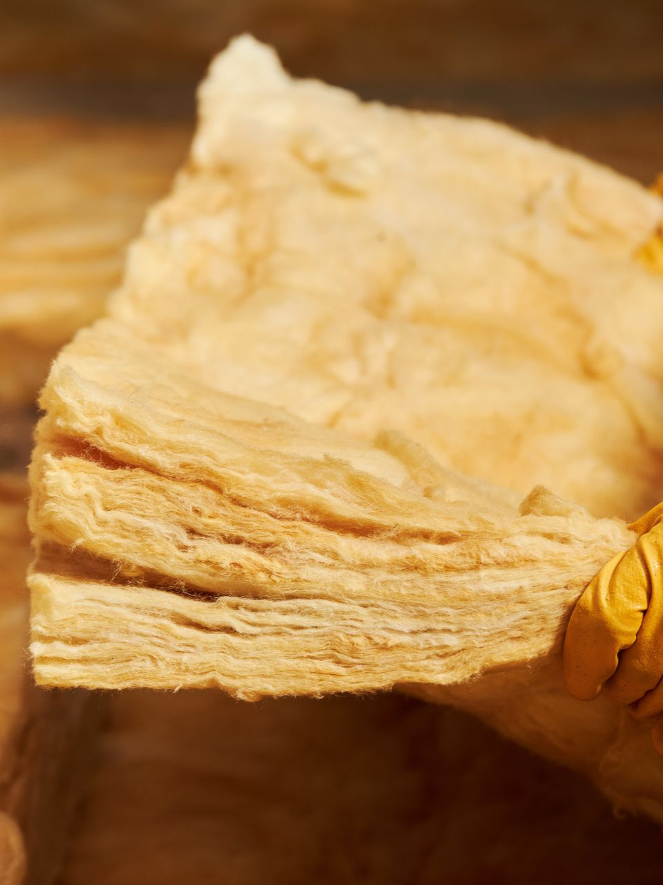 Gros plan d'un matériau isolant jaunâtre et fibreux, probablement destiné à la construction ou à la rénovation domiciliaire.