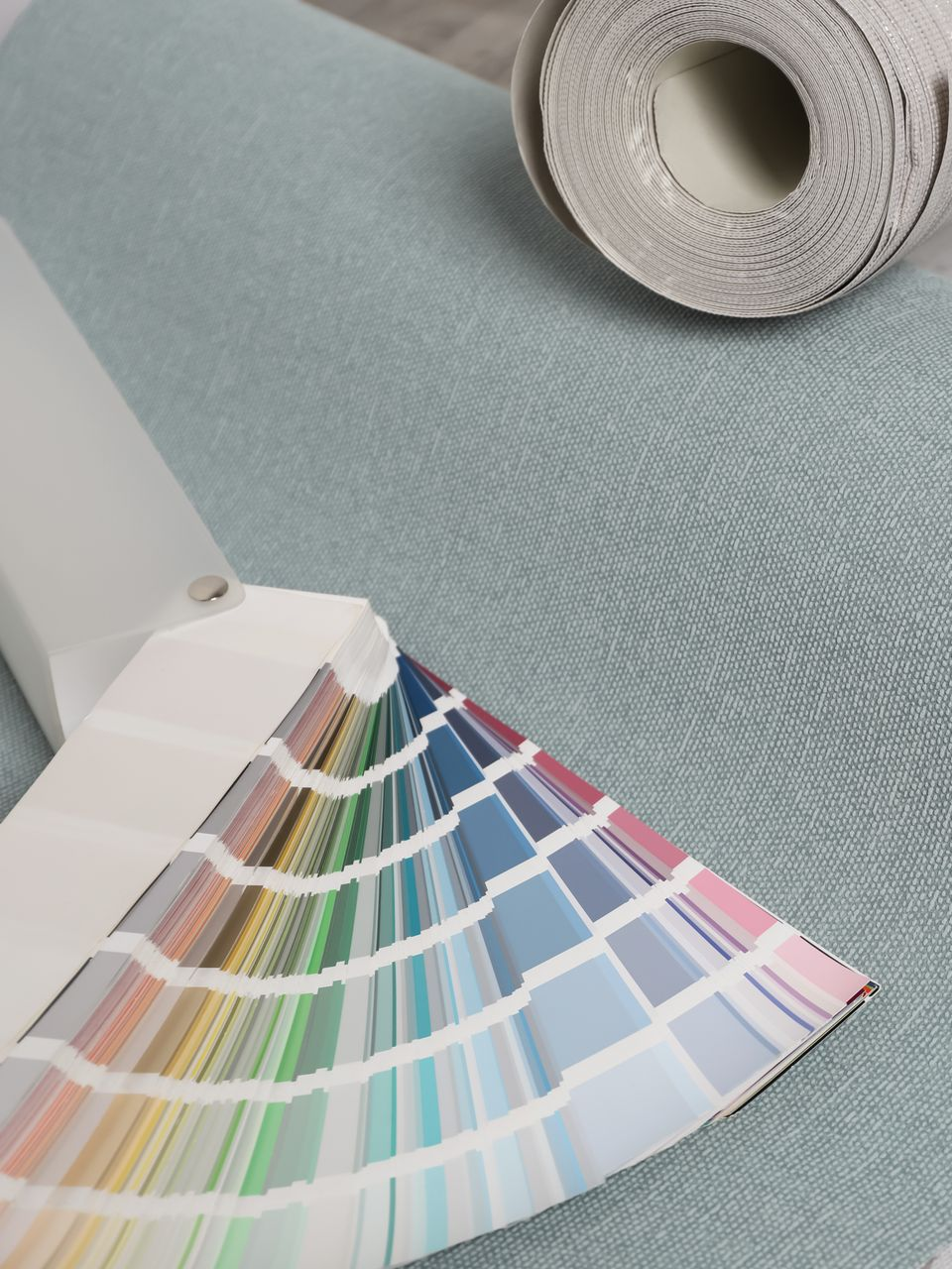 Palette de couleurs déployée sur une surface texturée bleu clair, avec un rouleau de papier peint en arrière-plan.