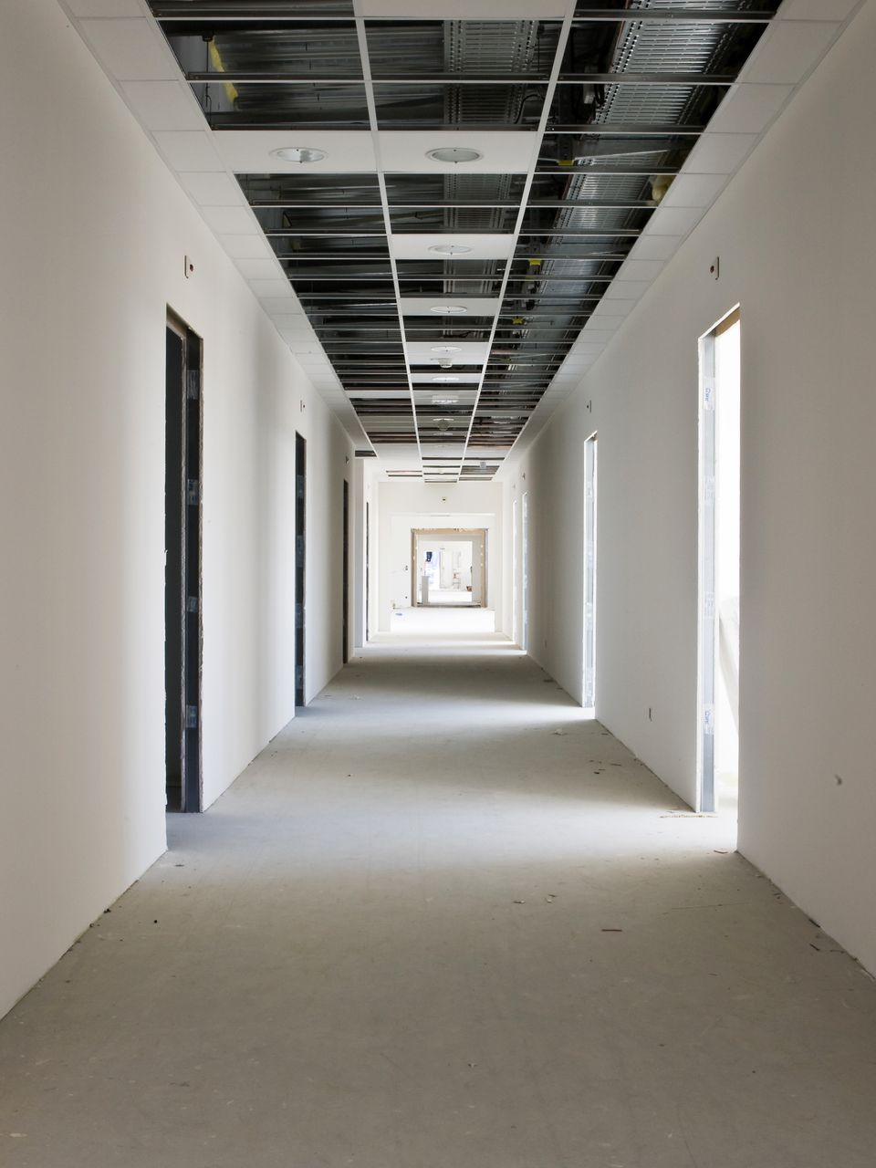 Couloir vide en construction, murs blancs, grille de plafond apparente.