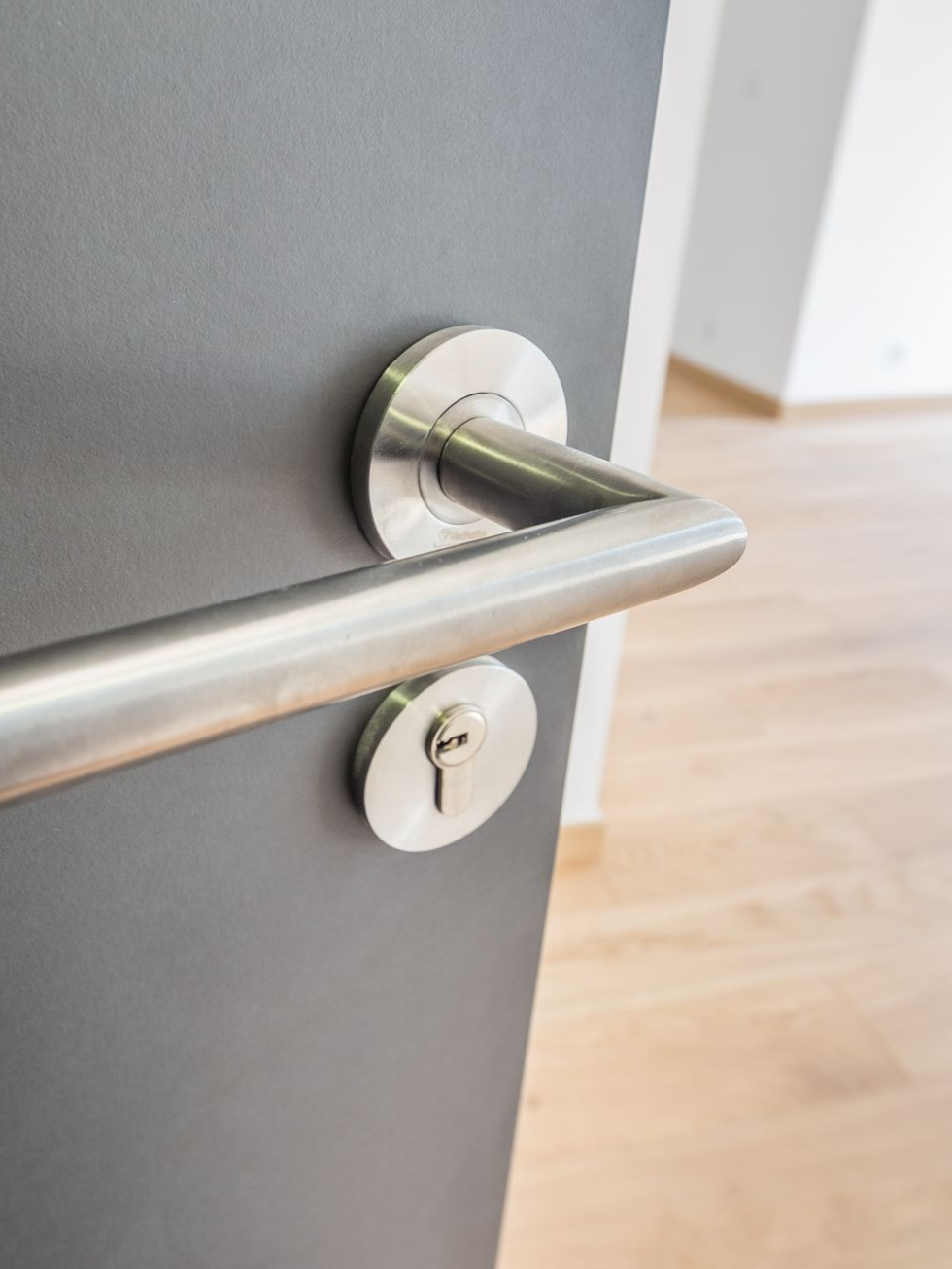 Poignée de porte argentée sur une porte grise ; la porte est légèrement entrouverte, s'ouvrant sur un intérieur lumineux.