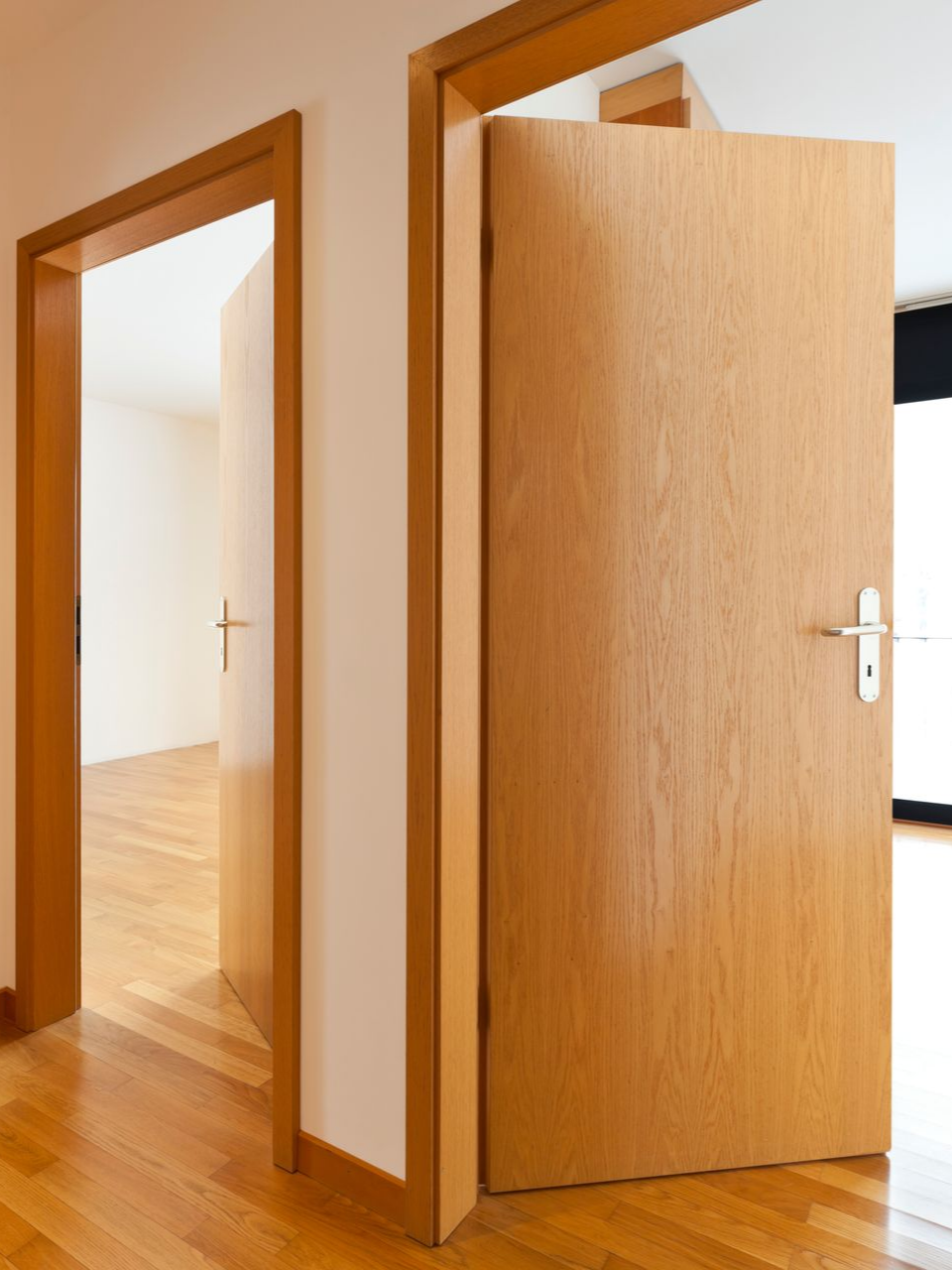 Trois portes en bois dans un intérieur lumineux, deux ouvertes, une fermée, avec un plancher en bois franc.