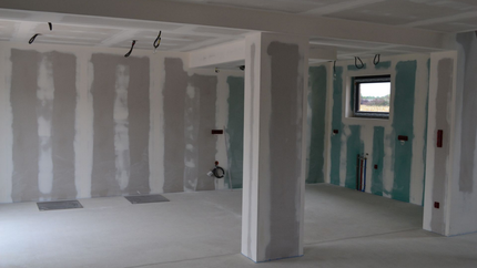Intérieur d'une pièce en construction ; cloisons sèches installées sur les murs et le plafond, fils exposés.