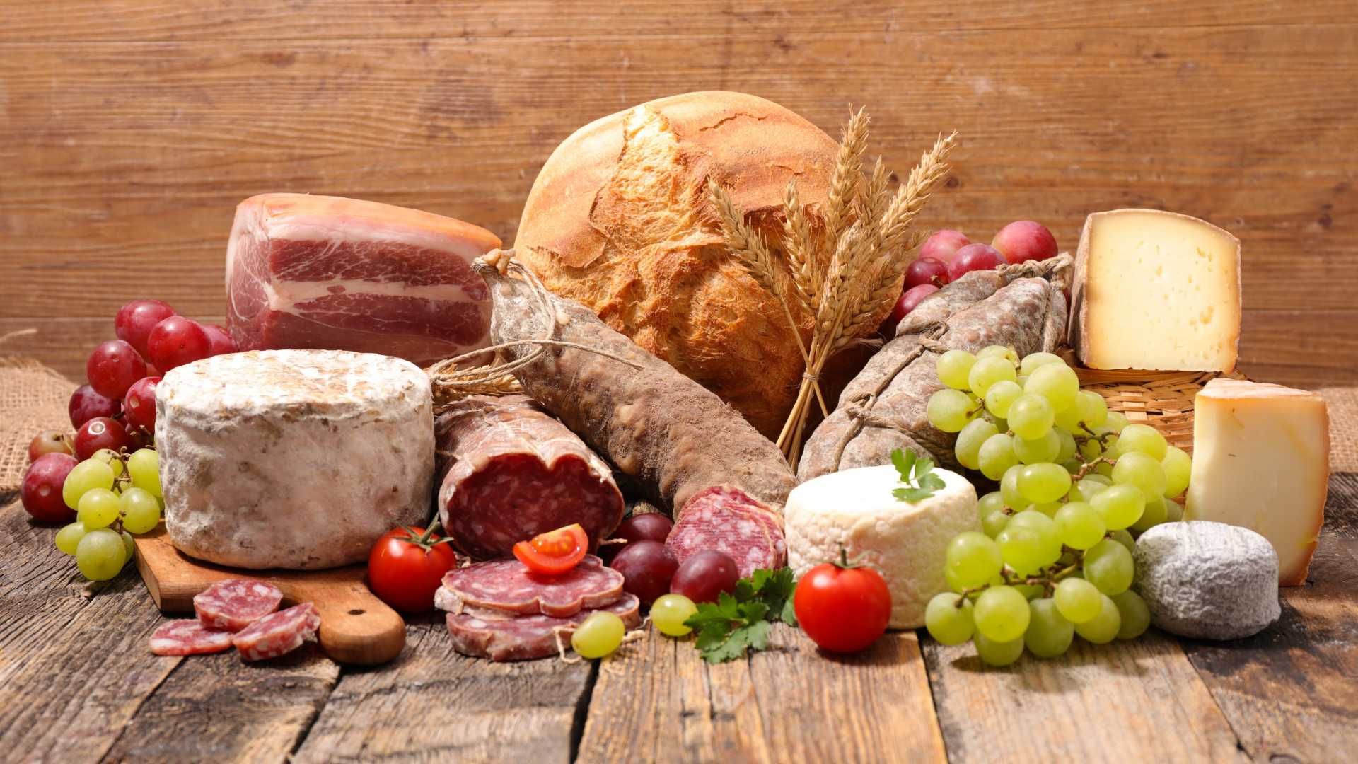 Una mesa de madera cubierta con una variedad de carnes, quesos, uvas y pan.