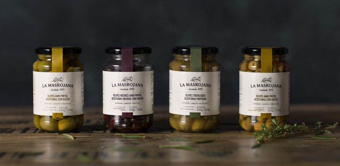 Cuatro frascos de aceitunas están sobre una mesa de madera.