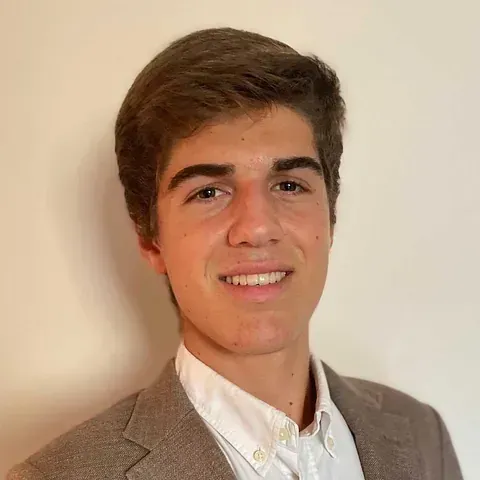 Un joven con traje y camisa blanca sonríe a la cámara.