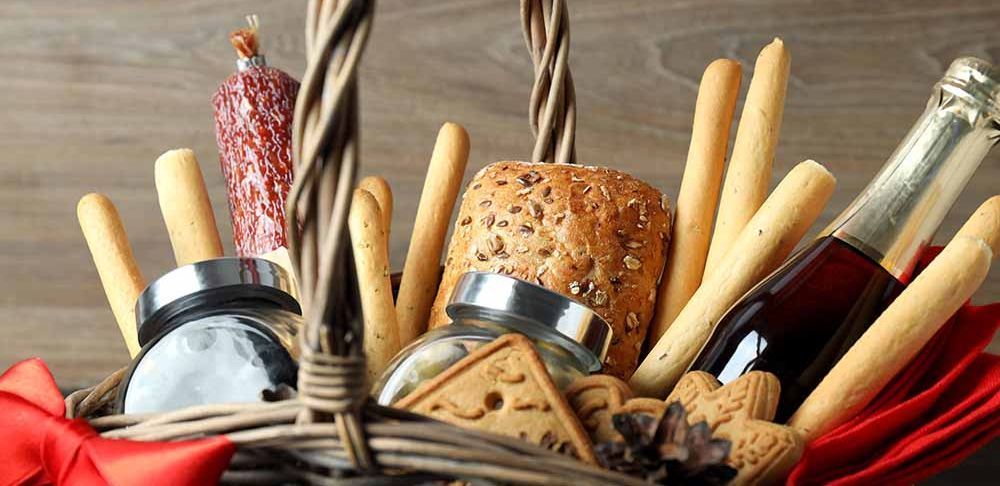 Una cesta de mimbre llena de palitos de pan, galletas, una botella de vino y un salami.