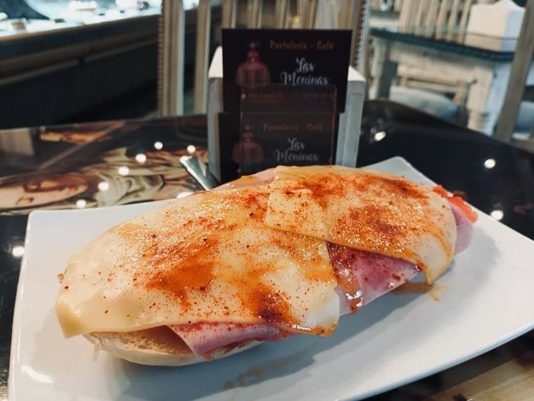 Sándwich en un plato blanco con jamón, queso y una pizca de pimentón, cerca de un tarjetero de restaurante.