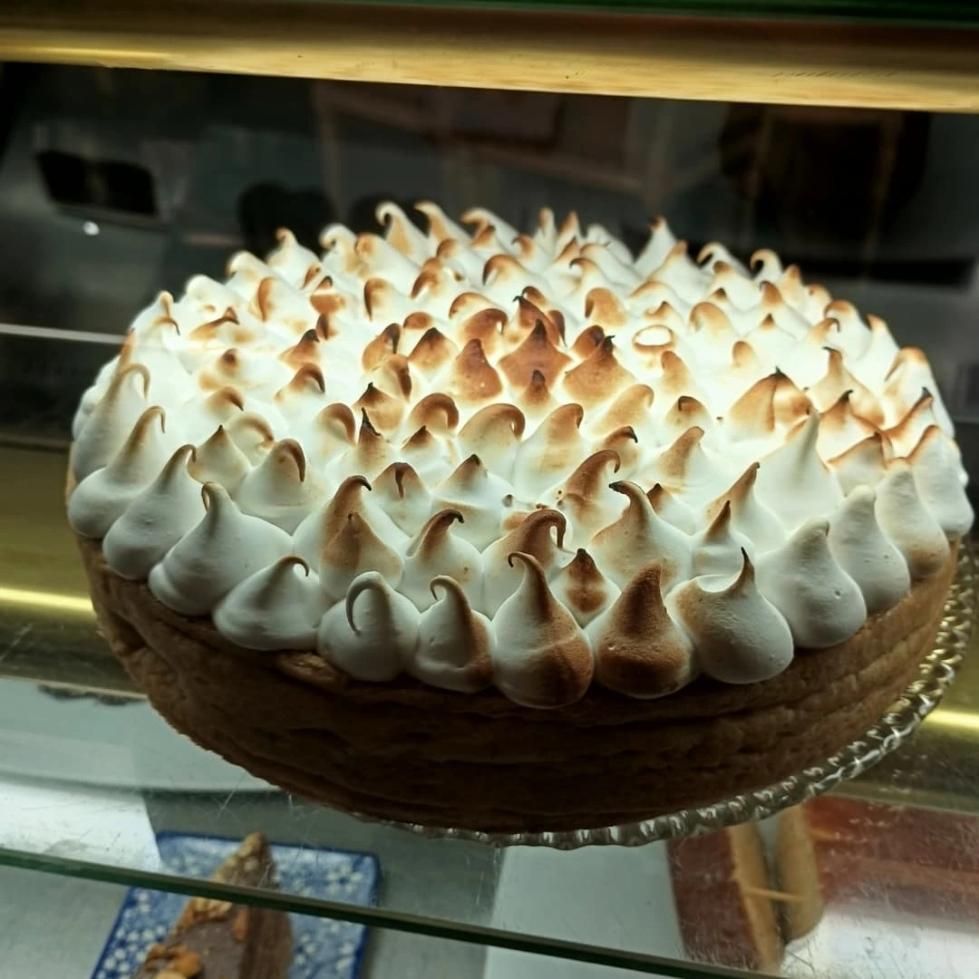 Tarta de merengue de limón en vitrina; picos blancos con puntas doradas.