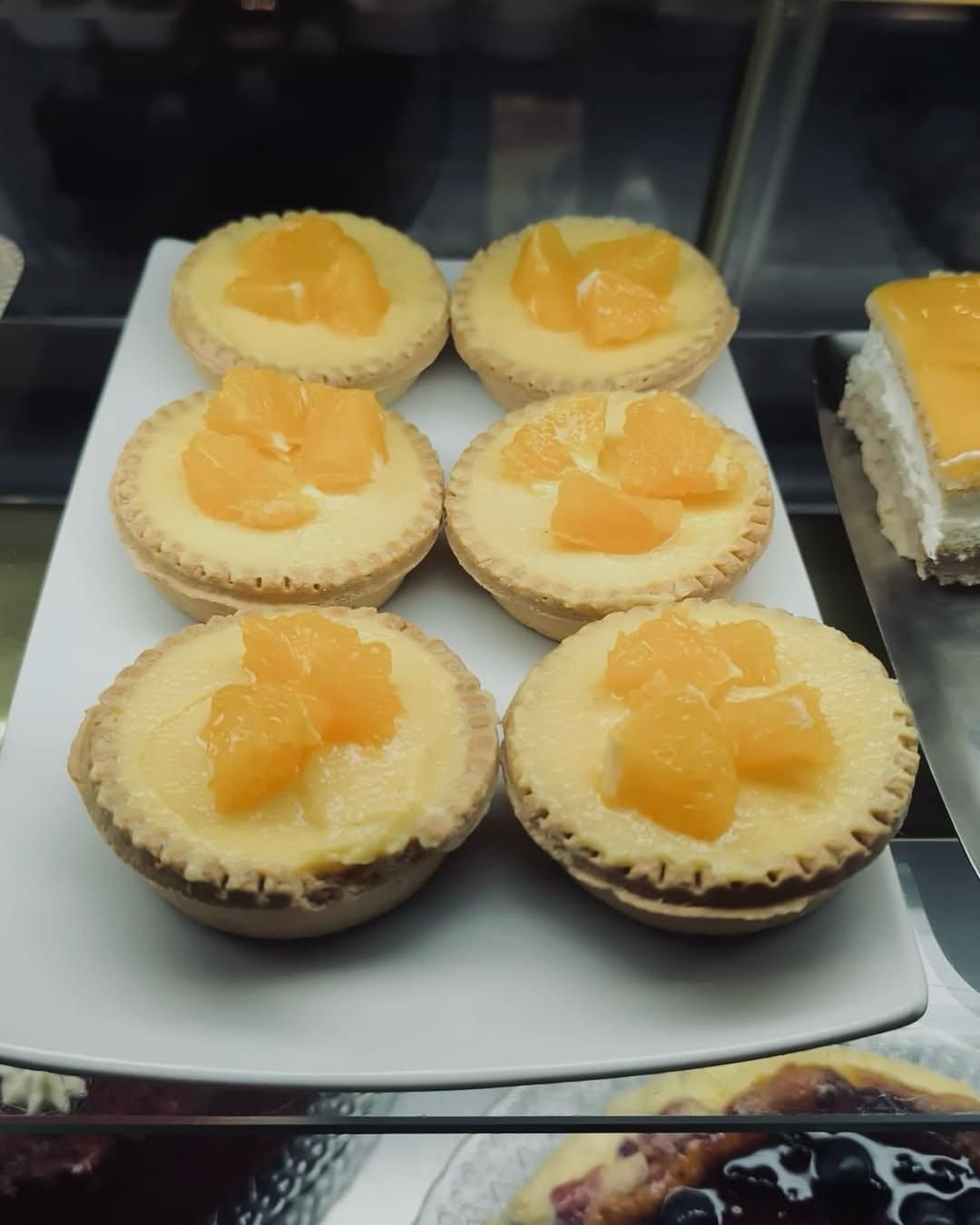 Seis tartas de crema de naranja dispuestas en un plato blanco, visibles dentro de una vitrina de cristal.