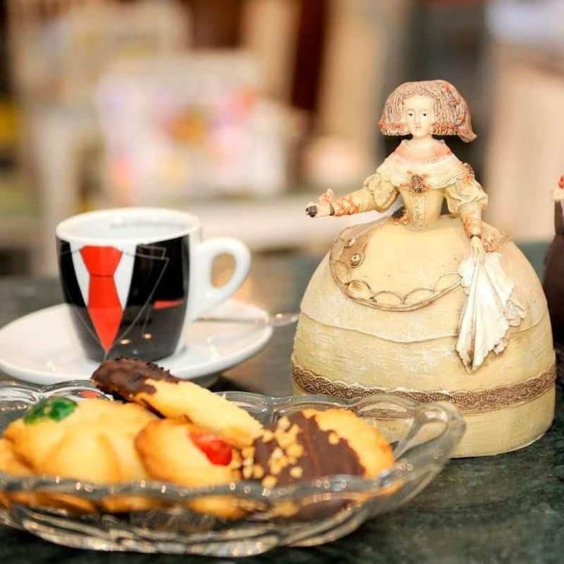 Taza de café, galletas y una figura decorativa sobre una mesa. La taza tiene un diseño de traje.