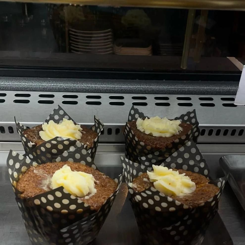 Cuatro cupcakes glaseados en envoltorios de lunares exhibidos detrás de un mostrador de vidrio.