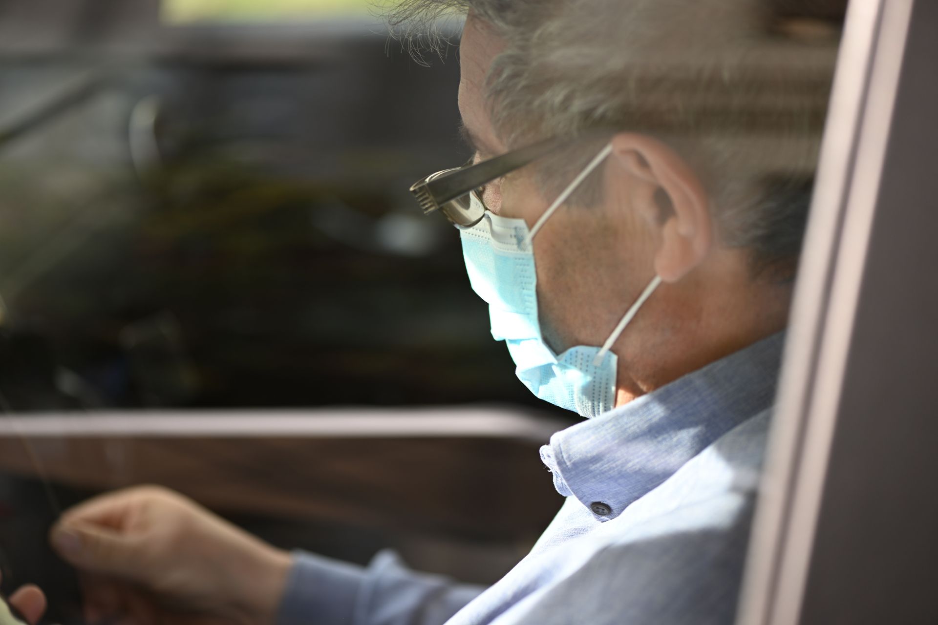 Un monsieur de profil portant un masque dans une automobile