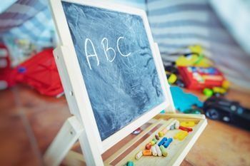 Caballete de pizarra infantil con el abecedario escrito con tiza y letras de juguete en la bandeja.