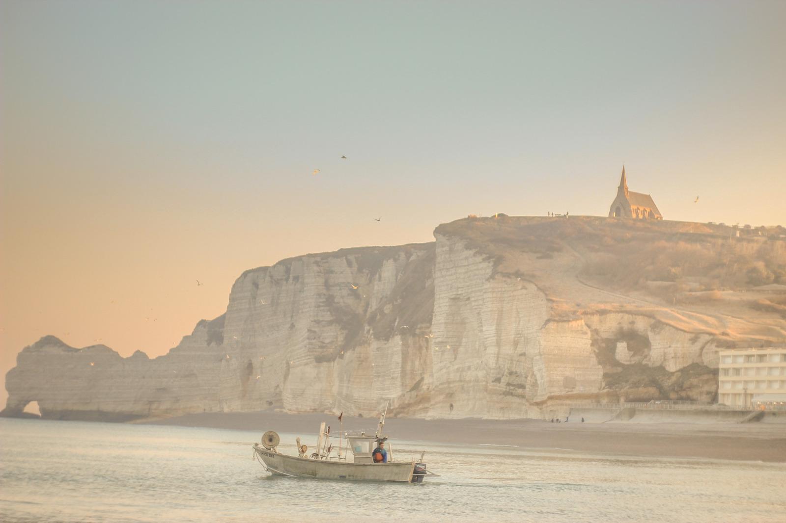Bateau sur l'eau, en fond une falaise avec un bâtiment type église