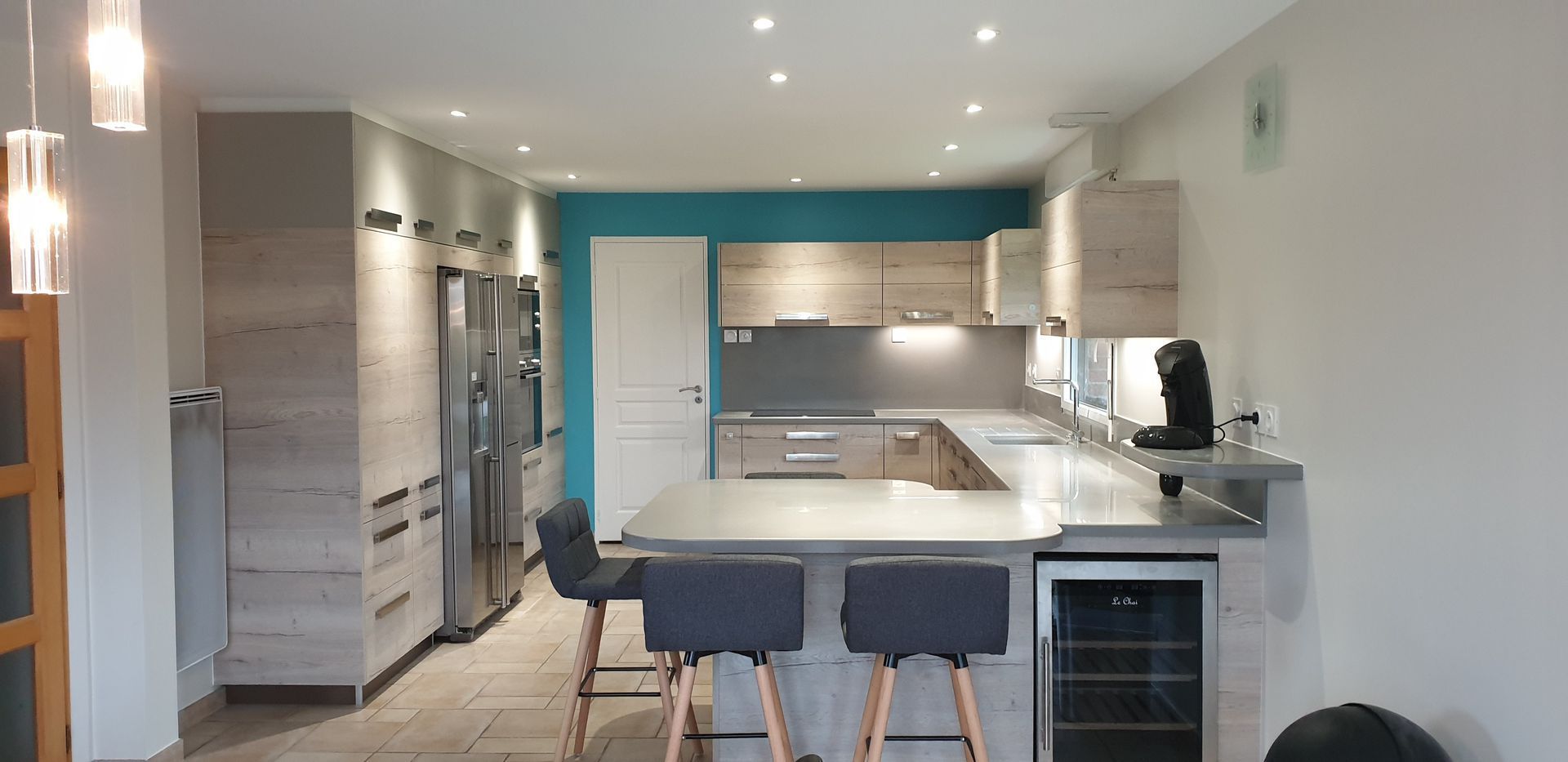 Cuisine moderne avec îlot blanc, armoires grises, mur d'accent turquoise et tabourets de bar.