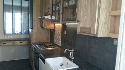 Cuisine moderne étroite avec placards en bois, crédence en carrelage foncé, cuisinière à gaz, évier et lave-linge près de la fenêtre.
