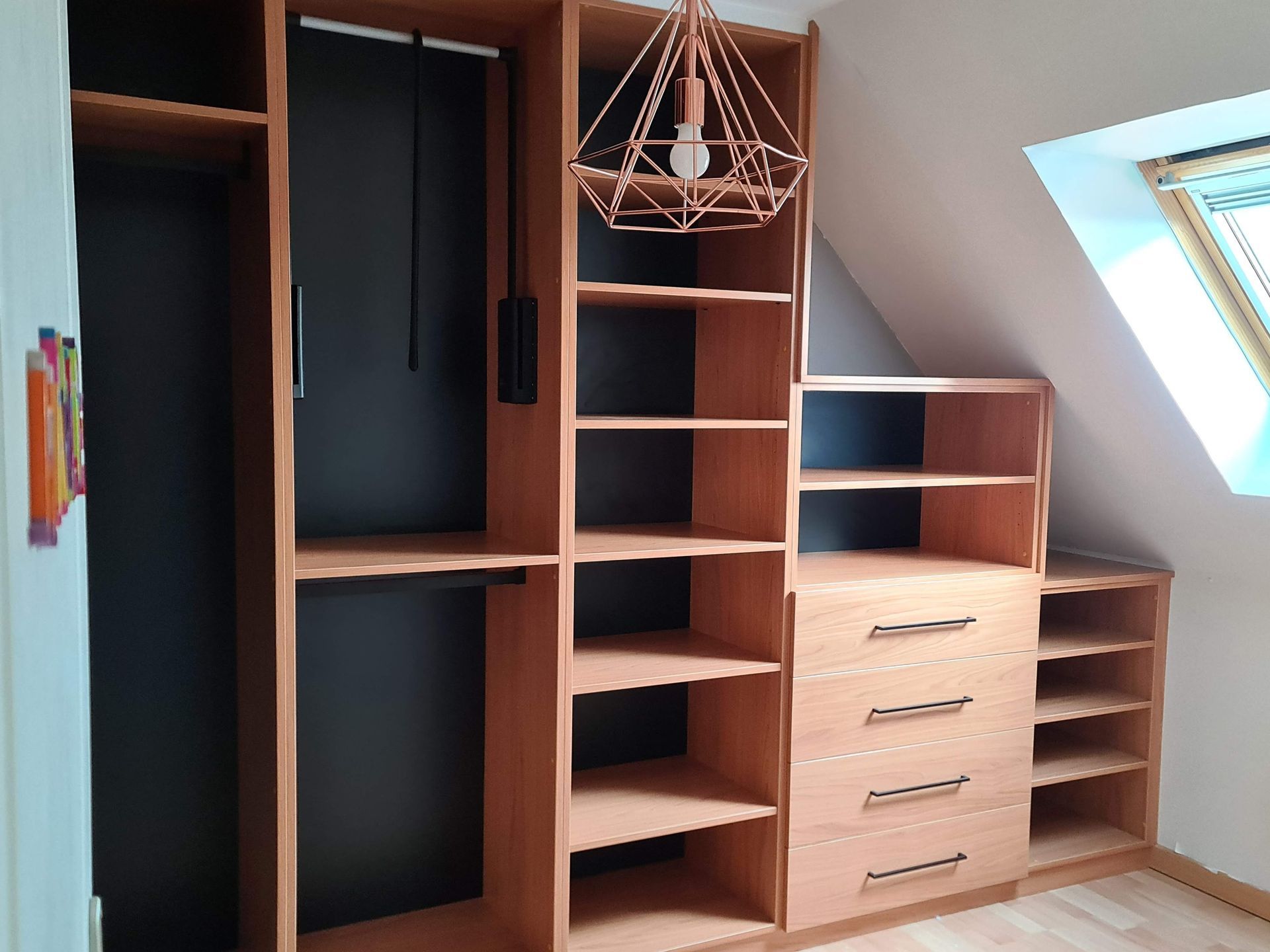 Placard intégré en bois avec étagères ouvertes, penderie noire, tiroirs et suspension lumineuse moderne sous un plafond mansardé
