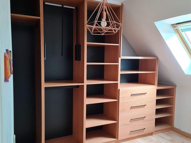 Placard intégré en bois avec étagères ouvertes, penderie noire, tiroirs et suspension lumineuse moderne sous un plafond mansardé