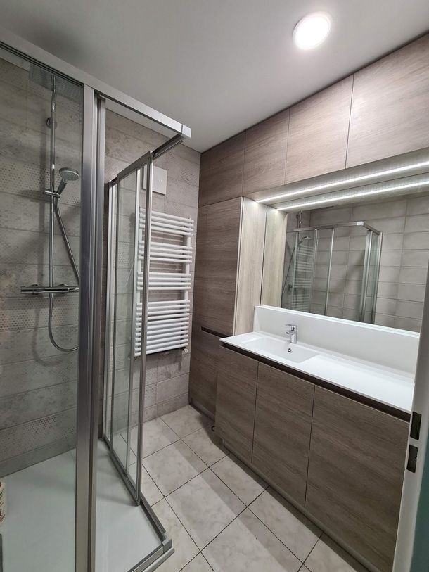 Salle de bains moderne avec douche en verre, grand miroir, lavabo blanc et sol carrelé