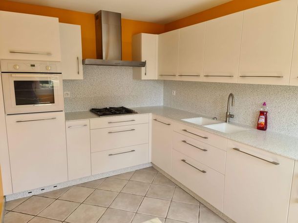 Cuisine moderne blanche avec placards, four encastré, plaque de cuisson, carrelage au sol et murs orange.
