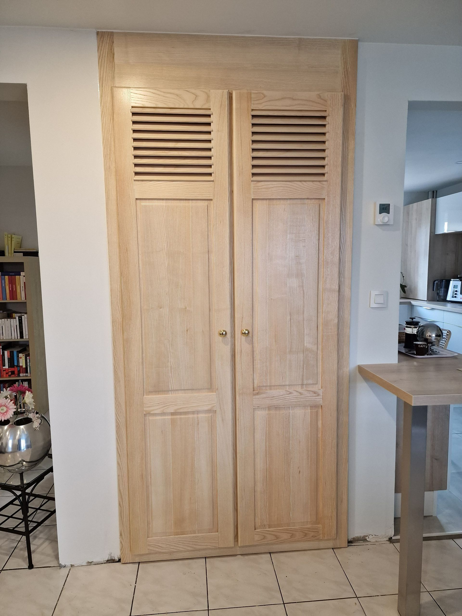 Double porte à persiennes en bois au centre d'un couloir intérieur.
