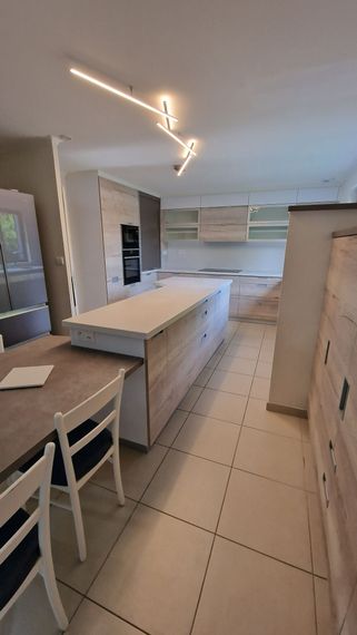 Cuisine blanche moderne avec îlot central, sol carrelé, tabourets de bar et éclairage au plafond