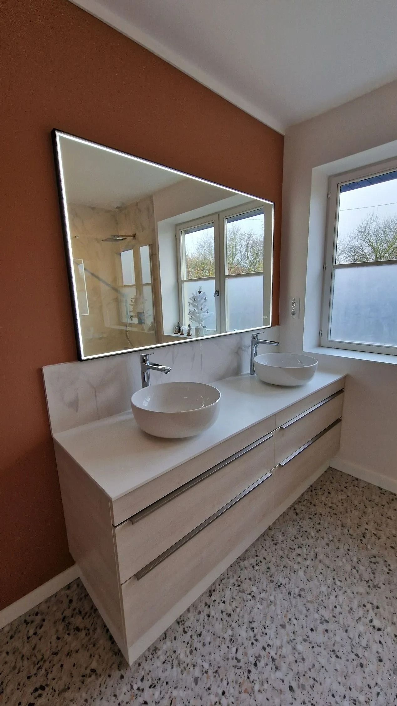 Meuble-lavabo moderne avec vasque, grand miroir et fenêtre à côté d'un mur en terre cuite