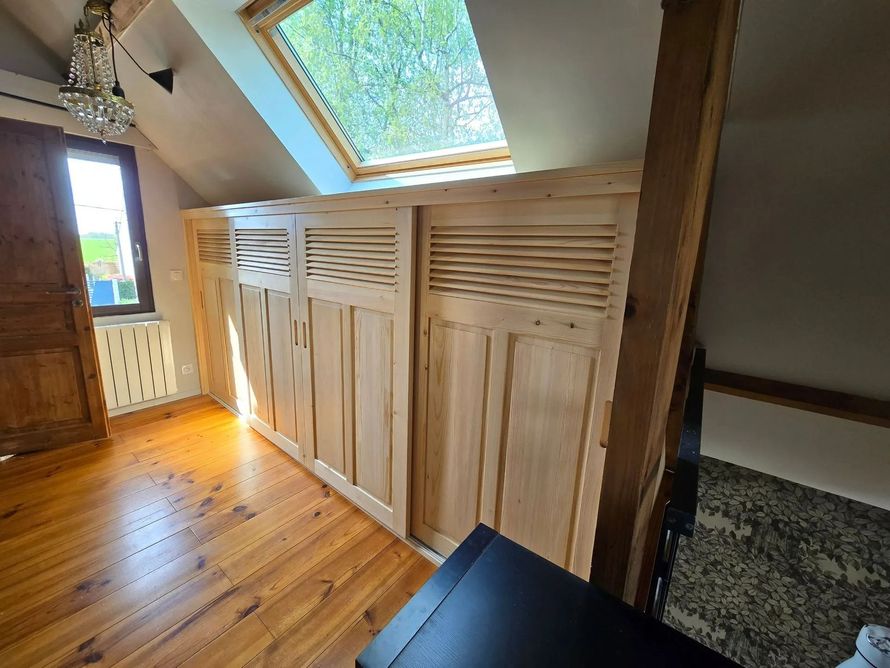 Couloir mansardé avec plancher en bois, portes de placard à lattes et fenêtres de toit.