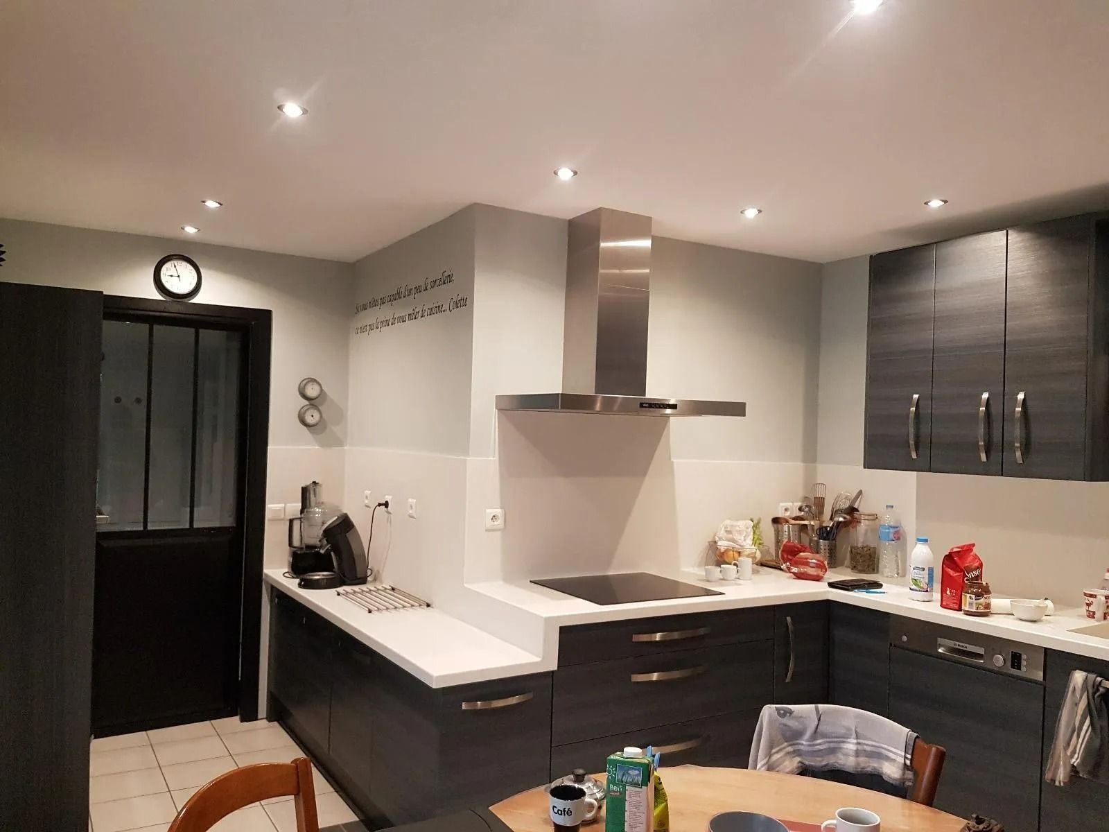 Cuisine moderne avec placards foncés, plans de travail blancs et électroménager en inox sous éclairage encastré