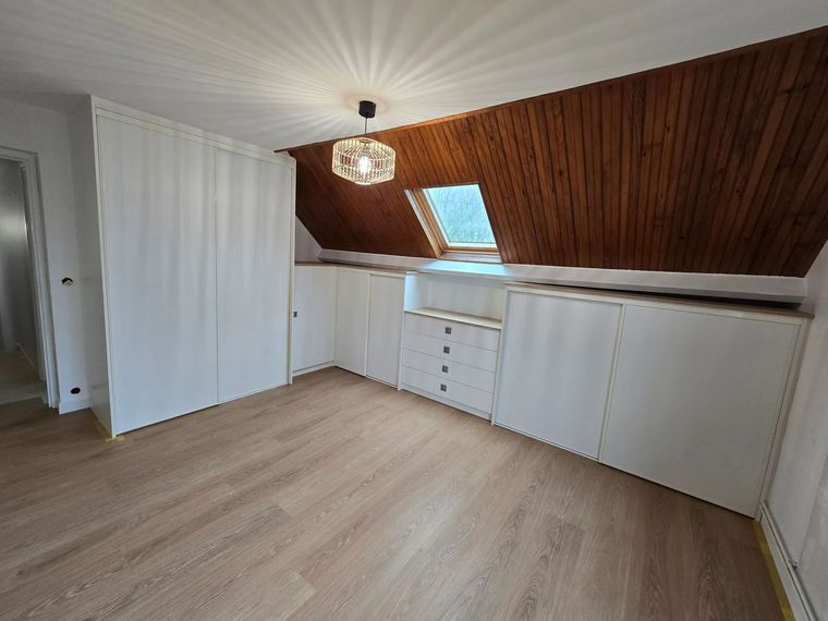 Grenier vide avec plafond mansardé lambrissé, puits de lumière, placards blancs et parquet clair