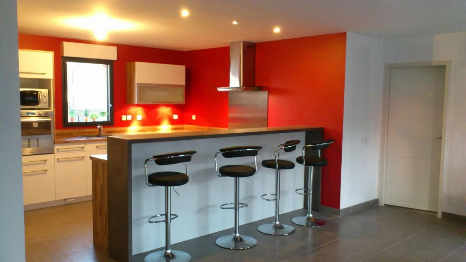 Cuisine moderne avec un mur d'accent rouge, un bar pour le petit-déjeuner et quatre tabourets noirs.