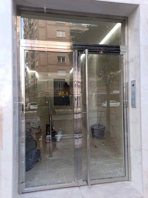 Primer plano de una puerta de acero inoxidable con tirador vertical y placa de empuje, junto a una pared revestida de vidrio.