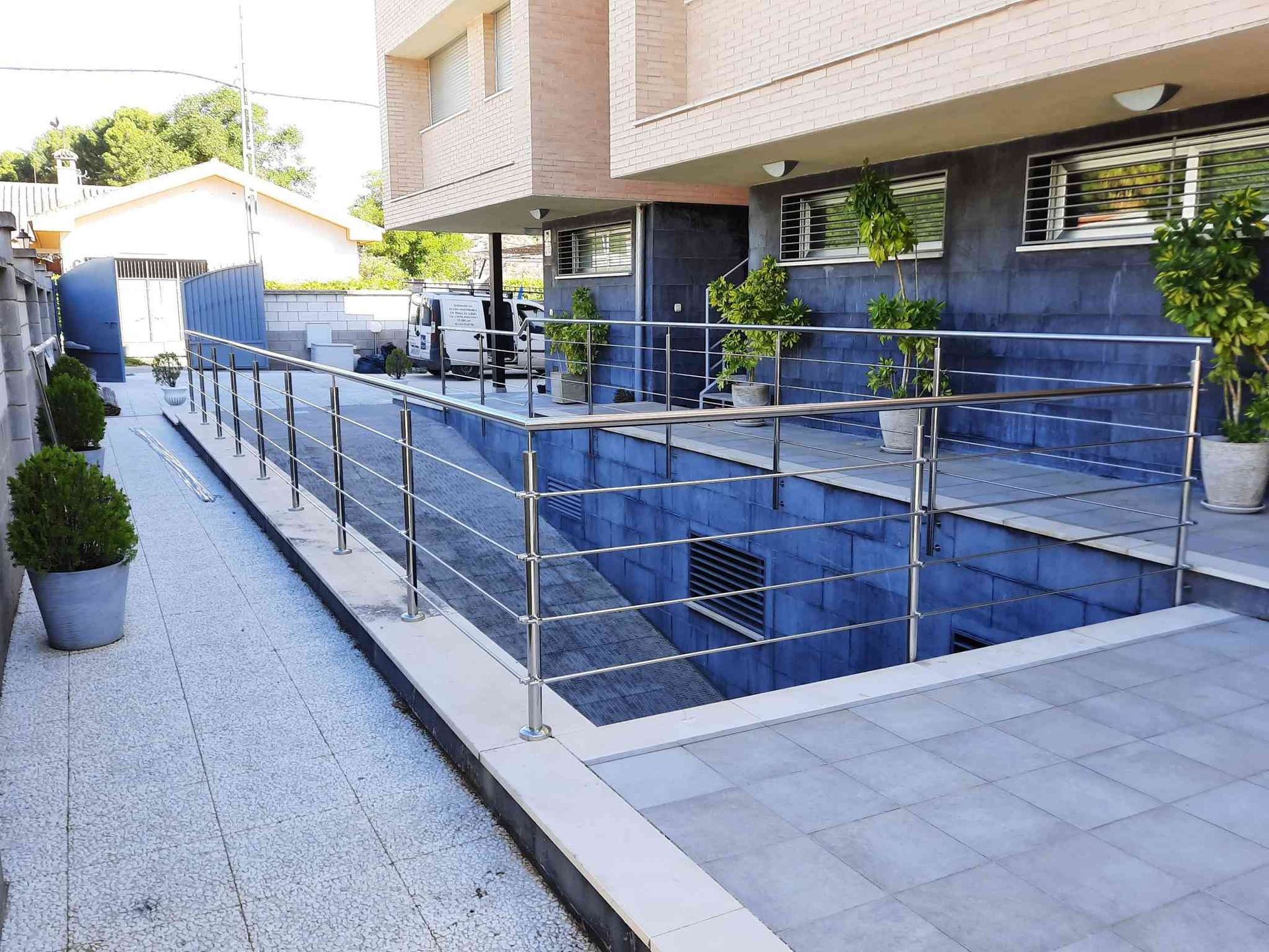 Exterior de un edificio con rampa para sillas de ruedas. Se ven pasamanos de acero inoxidable y plantas en macetas.