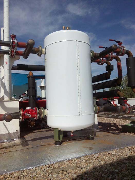 Un gran tanque blanco está al lado de un montón de tuberías.