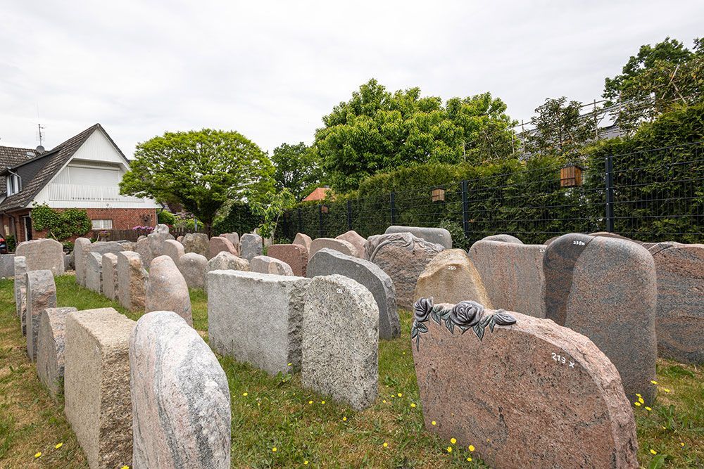 Eine Reihe von Gräbern auf einem Friedhof mit einem Haus im Hintergrund