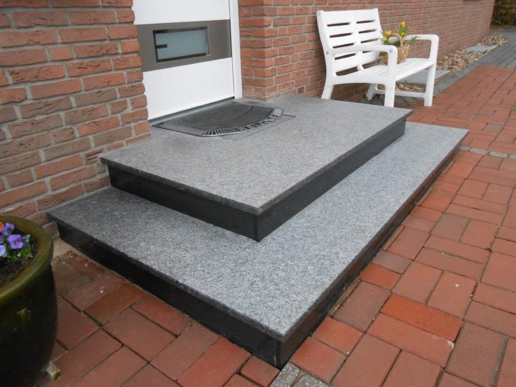 Eine weiße Bank steht auf einem gepflasterten Gehweg neben einer Treppe, die zu einer Tür führt.