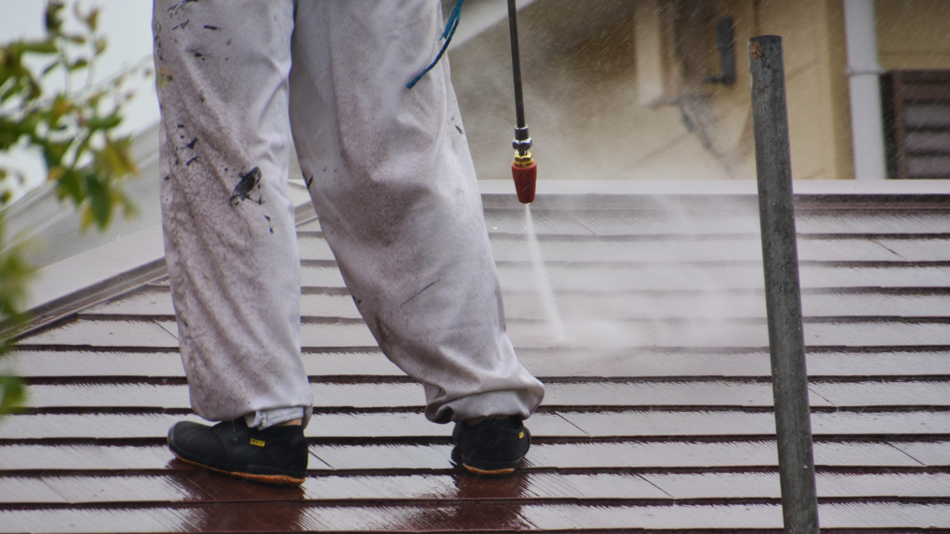 Une personne en combinaison blanche nettoie au jet d'eau un toit en bardeaux bruns.