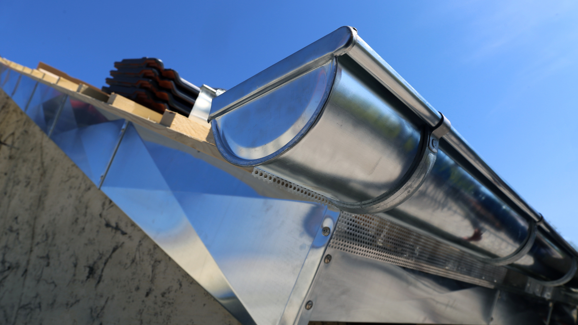 Gouttière métallique brillante sur un toit, ciel bleu en arrière-plan.