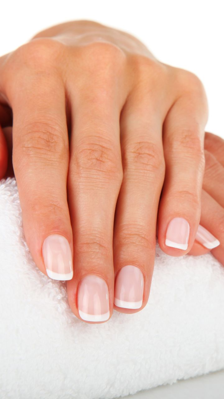 Mains d'une femme aux ongles manucurés à la française reposant sur une serviette blanche.