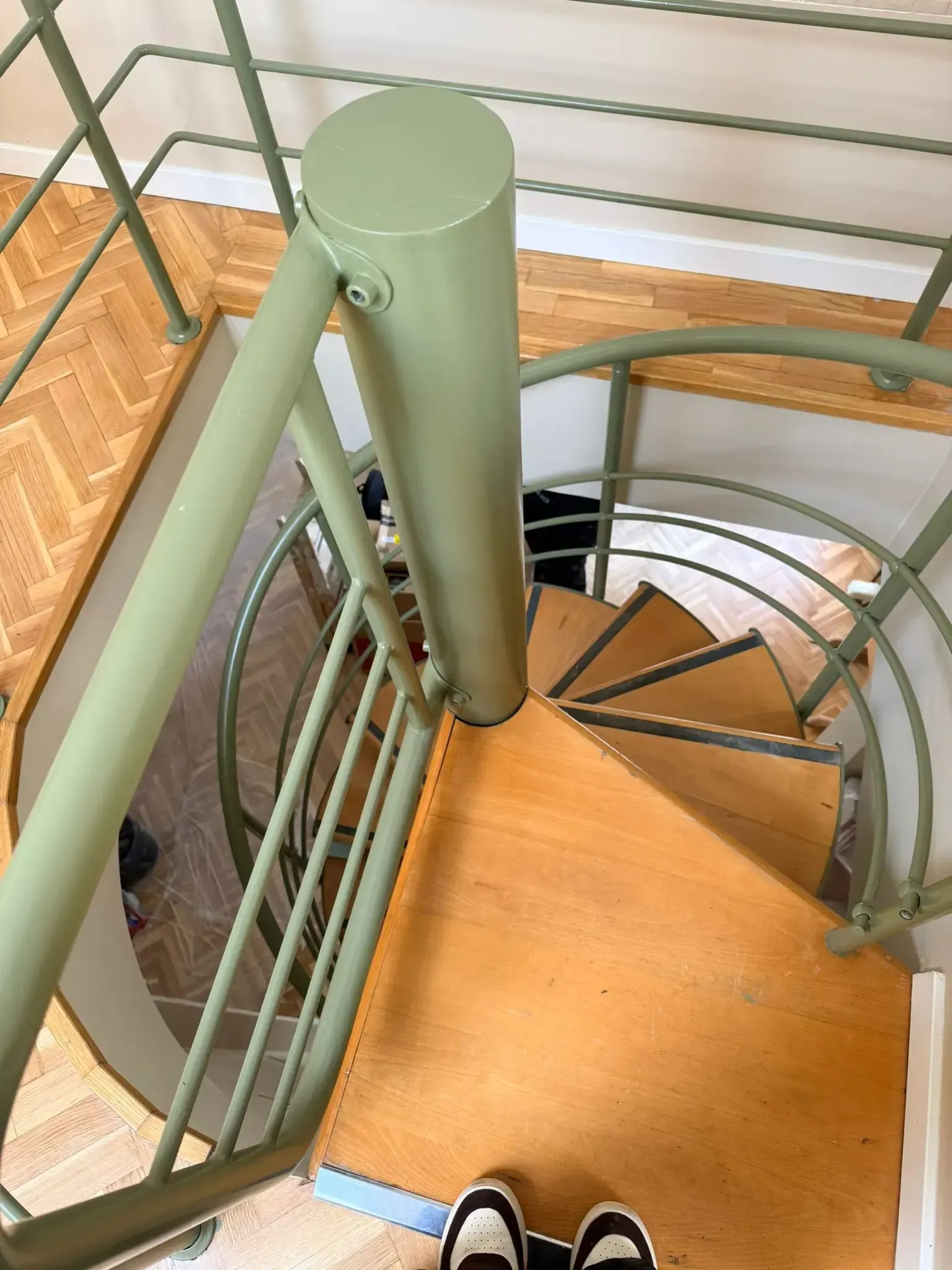 Escalera de caracol con barandilla de metal verde y escalones de madera en un rincón interior.