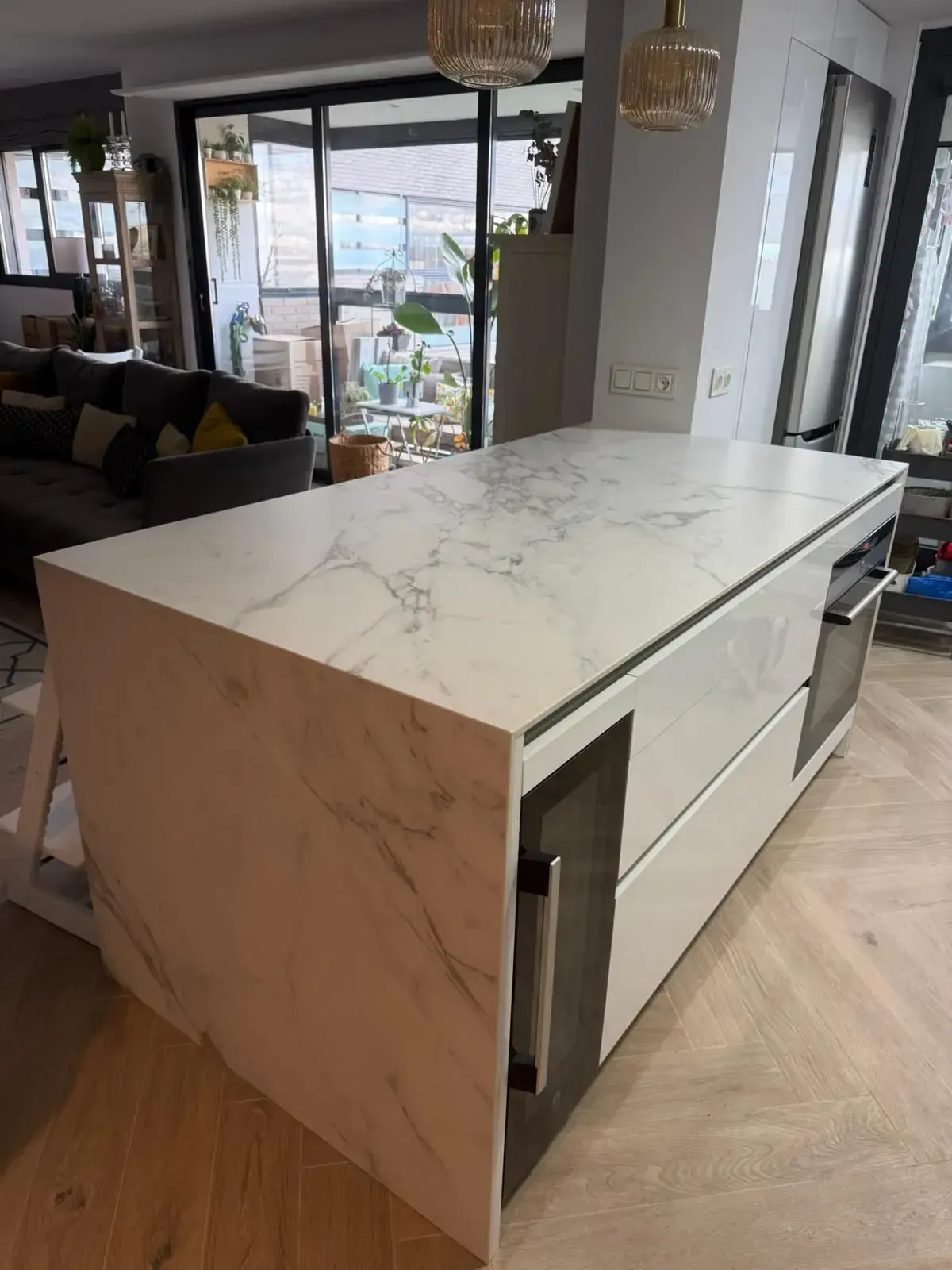 Moderna isla de cocina con encimera de mármol blanco y armarios de madera clara en una luminosa casa de planta abierta.