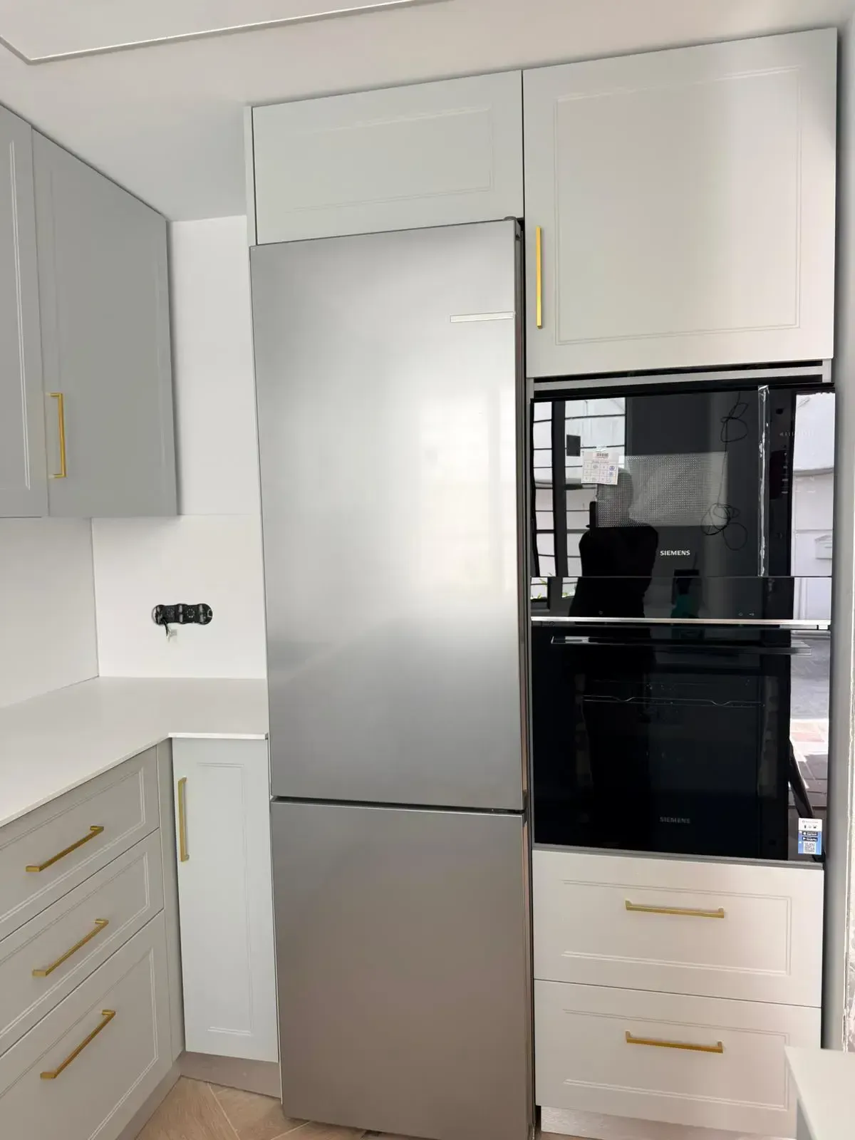 Cocina moderna blanca con refrigerador de acero inoxidable y horno empotrado negro.