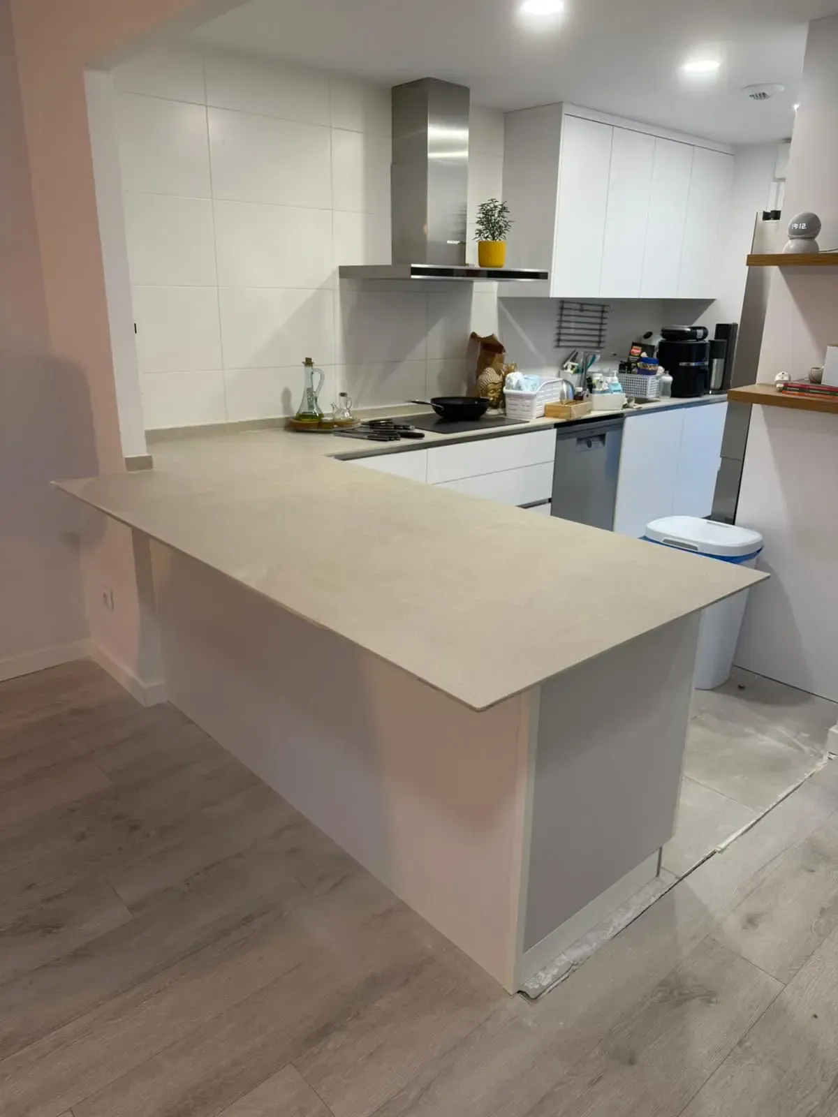 Cocina moderna con península beige, armarios blancos y suelo de madera clara.
